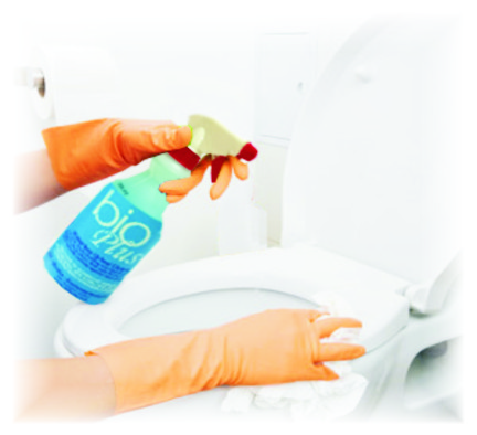 Hands in orange gloves spraying toilet cleaner onto a toilet with a spray bottle and wipe in a bathroom.